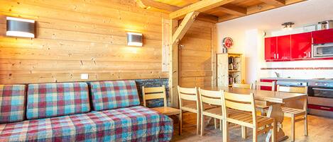 Un interior de madera con sofá, mesa de comedor, sillas y una zona de cocina con armarios rojos.