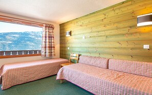 A room with two beds, a window with a view of a mountain, and a wooden wall. - Residence Le Beauregard - Vacanceole (La Léchère)