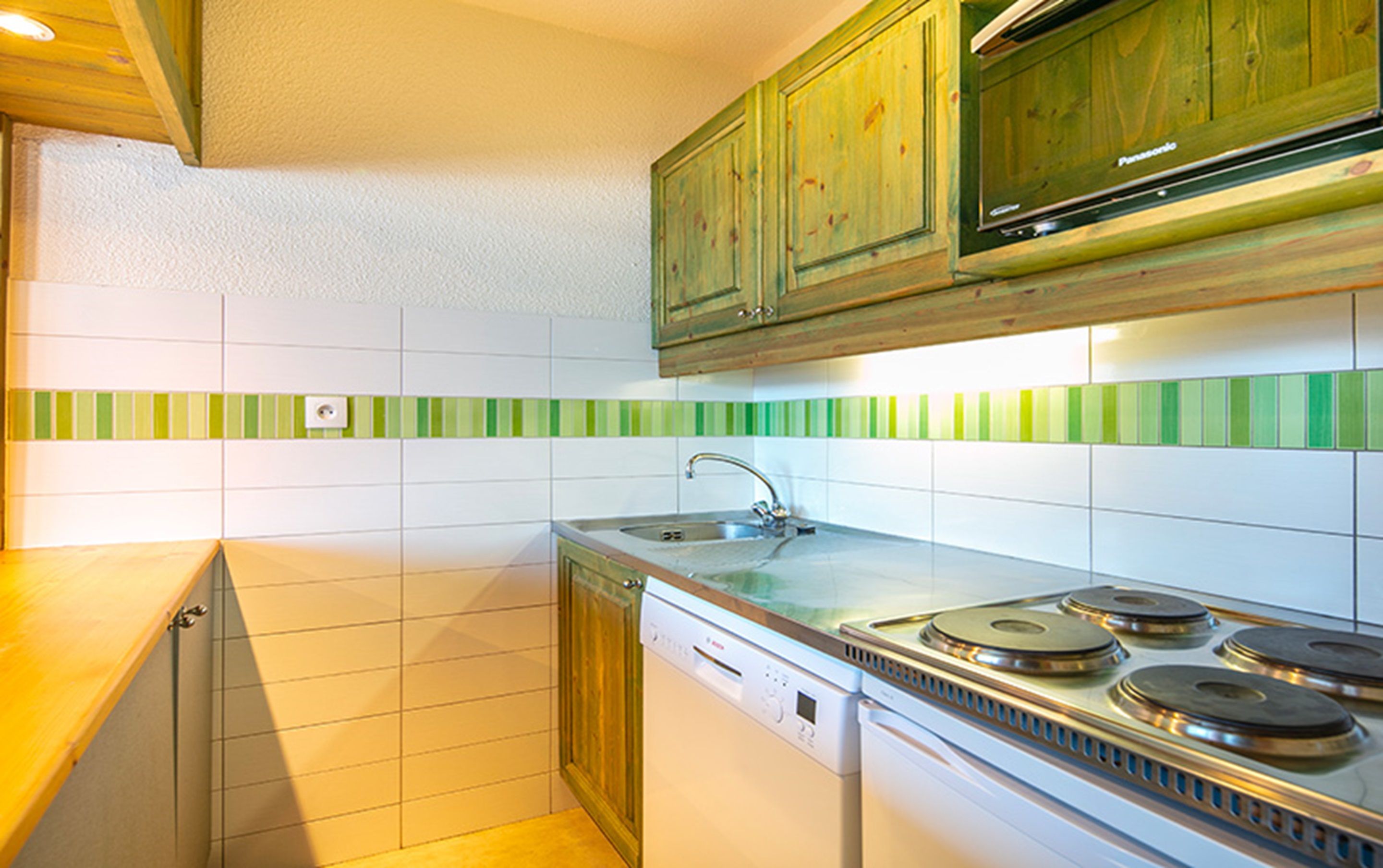 A compact kitchen with a dishwasher, stove, and green-striped backsplash.