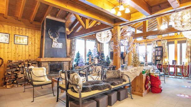 A cozy log cabin interior with a fireplace, wooden walls, and a festive Christmas tree.
