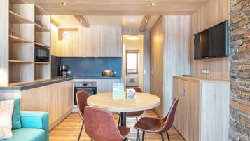 Een moderne keuken met houten kastjes, een eettafel met stoelen, een bank en een flatscreen televisie bevestigd aan een stenen muur.