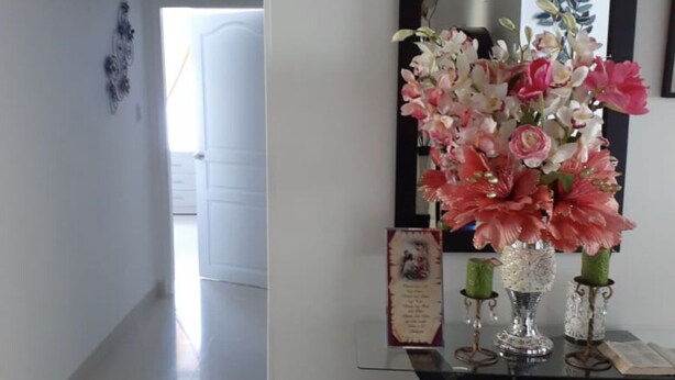 A hallway with a glass table displaying a floral arrangement, a framed picture, and a small plaque. - Remodeled Gorgeous Apartment on Beach (Cartagena)
