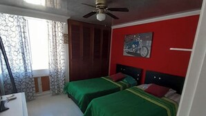 A bedroom with two beds, a ceiling fan, a red wall with a bicycle painting, and a window with patterned curtains. - Remodeled Gorgeous Apartment on Beach (Cartagena)