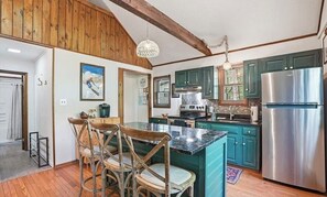 A kitchen with wooden beams, teal cabinets, a stainless steel refrigerator, and a dining area with a wooden table and chairs.