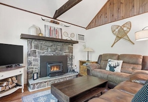 A cozy living room with a stone fireplace, leather sofa, and a television.