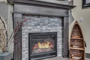 A fireplace with a tiled surround, a wooden shelf with books, and a vase with branches.