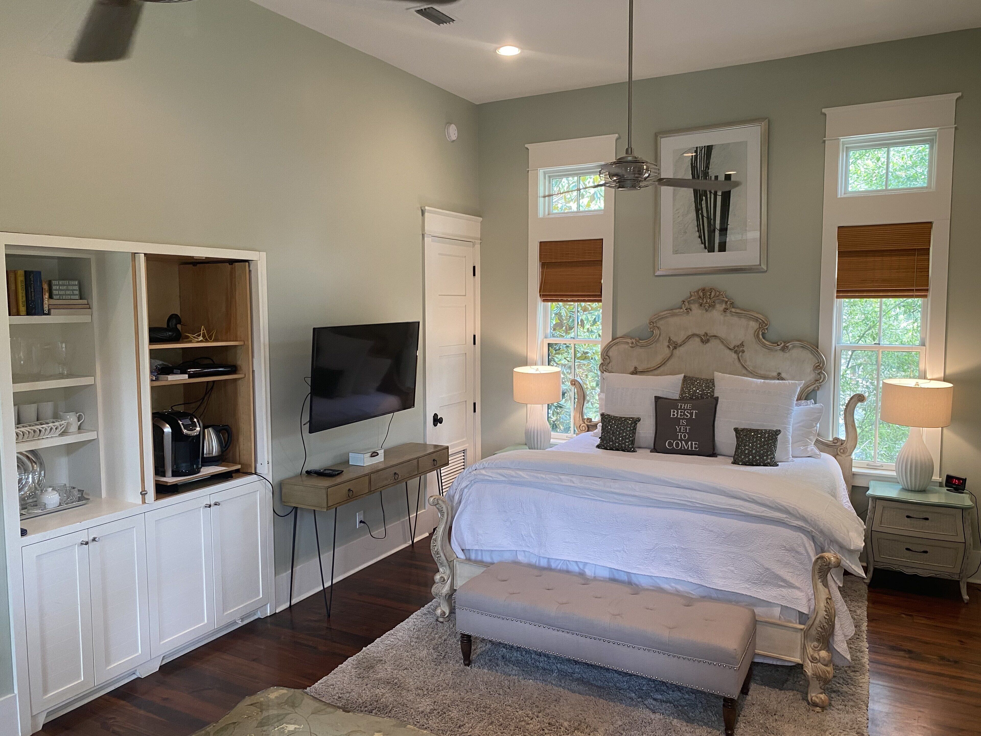 A bedroom with a bed, bedside lamps, a television, a wardrobe, and a ceiling fan.