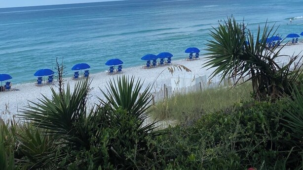 Een strand met wit zand, blauwe parasols en een heldere lucht.