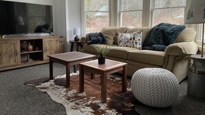 Un salon chaleureux avec un canapé, deux petites tables en bois, un téléviseur et un tapis en peau de vache.