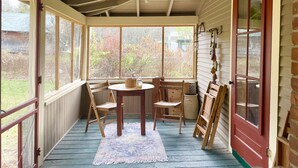 Une véranda avec un plafond en bois, de grandes fenêtres, une table ronde et des chaises.