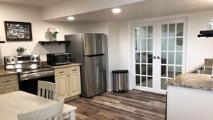 Una cucina moderna con elettrodomestici in acciaio inossidabile, un'area pranzo con tavolo e sedie in legno e una porta scorrevole in vetro che dà su un soggiorno.