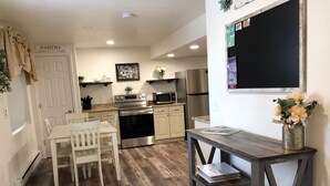 Una cucina moderna con pavimento in legno, elettrodomestici in acciaio inossidabile, un'area pranzo con sedie bianche e un piccolo tavolo con un vaso di fiori.
