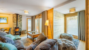 Una sala acogedora con chimenea de piedra, paredes de madera y ventanas grandes.