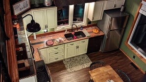 A compact kitchen with wooden cabinets, a sink, a refrigerator, and a dining area with a table and chairs. - Vista Getaway - Secluded country cabin, with wrap around porch and patio. (Klingerstown)