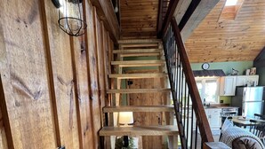 A wooden staircase with a metal railing, leading to a kitchen area with a refrigerator and a dining table. - Vista Getaway - Secluded country cabin, with wrap around porch and patio. (Klingerstown)
