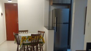 A dining area with a table and chairs, a refrigerator, and a door. - New apartment in Canto do Forte with ocean view, close to the beach. (PRAIA GRANDE)