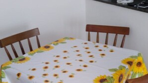 A dining table with a sunflower tablecloth, surrounded by wooden chairs. - New apartment in Canto do Forte with ocean view, close to the beach. (PRAIA GRANDE)