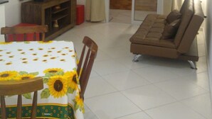 A living room with a sofa, a TV on a wooden stand, a dining table with chairs, and a sliding glass door leading to an outdoor area. - New apartment in Canto do Forte with ocean view, close to the beach. (PRAIA GRANDE)