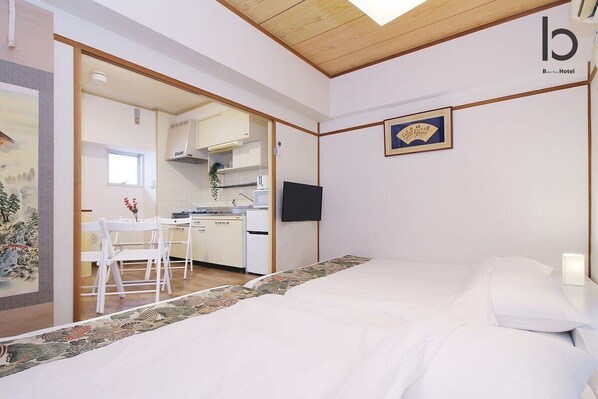 Quarto de hotel com cama, escrivaninha e cozinha compacta.