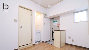 Una habitación de hotel con piso de madera, una puerta, un escritorio pequeño con un florero y una ventana.