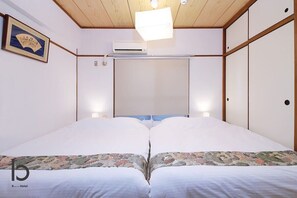 Quarto de hotel com cama, ventoinha no teto, ar condicionado fixado na parede e um quadro emoldurado.
