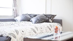 Un dormitorio moderno con un sofá gris, una colcha de estampado floral y una mesa de centro de vidrio con un pequeño objeto decorativo.