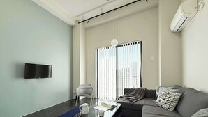 Una sala de estar moderna con un televisor de pantalla plana, un sofá, una mesa de centro y un ventanal con persianas.