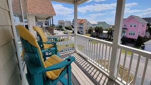 A covered porch with two turquoise chairs and a yellow cushion, overlooking a residential street with houses. - Surf City • Views, Views, and more Views! (Surf City)