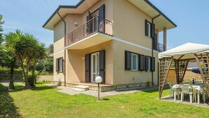 Una casa a due piani con un balcone, una zona relax esterna coperta e un giardino curato.