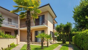 Edificio residenziale a due piani con balcone, vialetto in pietra e giardino curato.