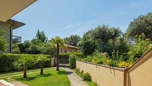 Un cortile con un vialetto in pietra, palme, arbusti e fiori vari.