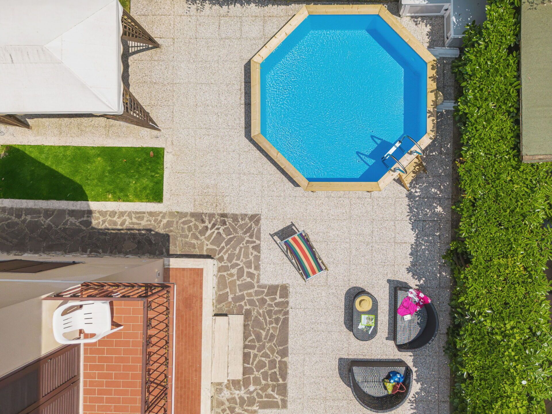 Uma piscina octogonal com deck de madeira, cercada por um pátio de pedra e um gramado verde.