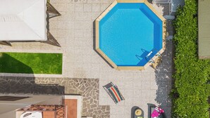 Una piscina ottagonale con un pontile in legno, circondata da un patio in pietra e un prato verde.