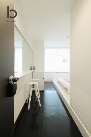A modern hotel room with a black floor, white walls, a large mirror, a small white stool, a bench, and a window providing natural light. - Studio apartment for 2 people with free wifi 101 (Hiroshima City)