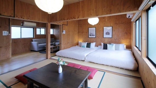 Une pièce de style japonais traditionnel, avec un sol recouvert de tatamis, un plafond bas en bois et un grand lit doté d’oreillers.