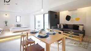 Una habitación de hotel moderna con una cama, una mesa de comedor con sillas, un sofá y un cuadro abstracto grande en la pared.