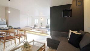 Una sala de estar moderna con sofá, una mesa de comedor con sillas, una zona de cocina y un televisor montado en la pared.
