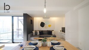 Una habitación de hotel moderna con comedor que incluye una mesa de madera dispuesta para cuatro, un sofá y un ventanal con vistas a la ciudad.