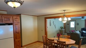 A dining area with a wooden table and chairs, a white refrigerator, and wooden cabinets. - Quiet Lake with Kayaks and Direct Beach Access! (Neshkoro)