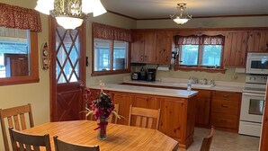 A spacious kitchen with wooden cabinets, a central island, and a dining area with a wooden table and chairs. - Quiet Lake with Kayaks and Direct Beach Access! (Neshkoro)