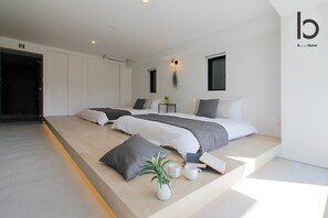 Una habitación de hotel moderna con dos camas, una mesita de noche pequeña, una planta y una lámpara fijada a la pared.