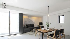A modern hotel room with a dining area, a sofa, and a TV. - b hotel 1002 Exclusive Urban Penthouse Stay (Hiroshima City)