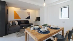 A modern living room with a dark grey sofa, a wooden dining table set with plates, cups, and a plant. - b hotel 902 Central Inner-Side Comfort Studio (Hiroshima City)