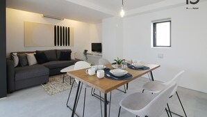 A modern living room with a dining area, a grey sofa, a wooden dining table, and a small window.
