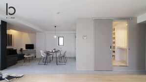 A modern hotel room with a living area, dining space, and a sliding door leading to a closet.
