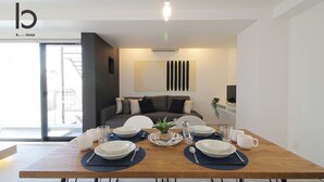 A modern dining area with a wooden table set for four, a sofa in the background, and a view of the outside through a glass door.