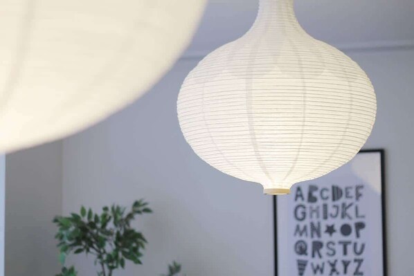 A hanging paper lantern with a grid pattern, a framed alphabet poster, and a potted plant.