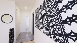 Un pasillo con un adorno de metal negro en la pared, un zapatero y una puerta que da a otra habitación.
