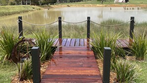 A wooden bridge leading to a pond surrounded by grass and trees.
