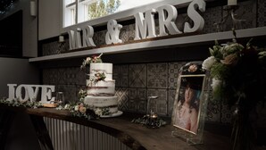A wedding reception setup with a tiered cake, a 'MR & MRS' sign, and a 'LOVE' sign.